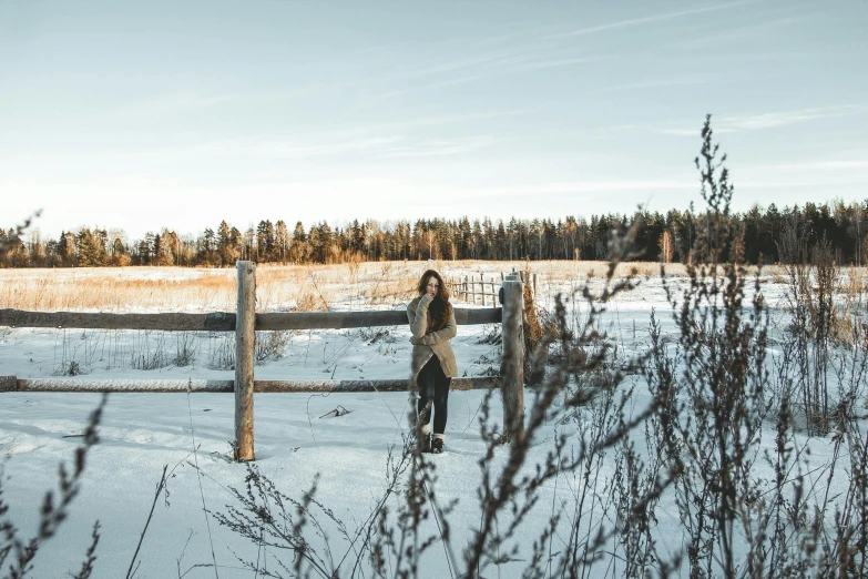 a woman standing in the snow behind a fence