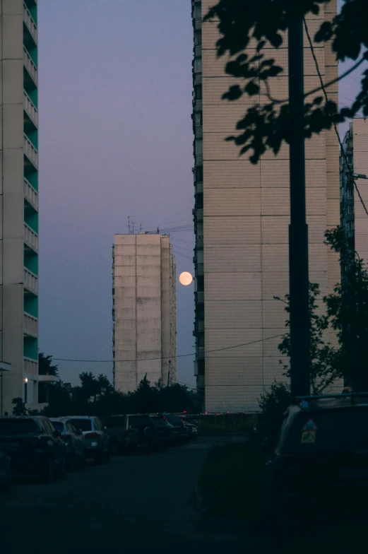 an orange eclipse is visible in the dark sky above the tall buildings