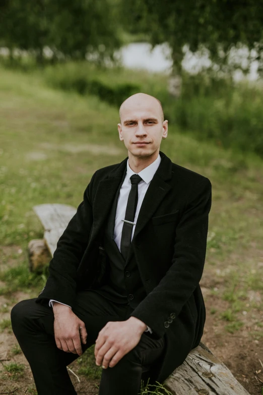 a man wearing a suit sits on a wood bench