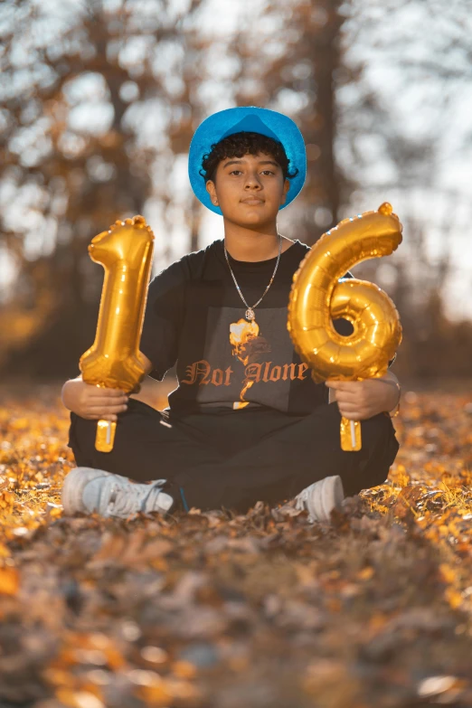 a young man with balloons and a hat sitting in the grass