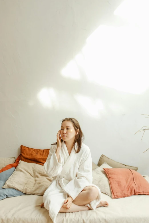 a woman in white robe sitting on the edge of a bed