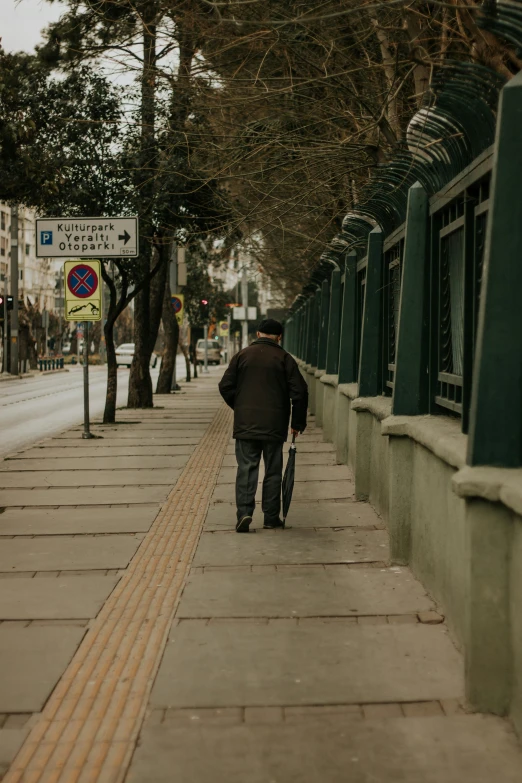 a man walking down the sidewalk between two trees