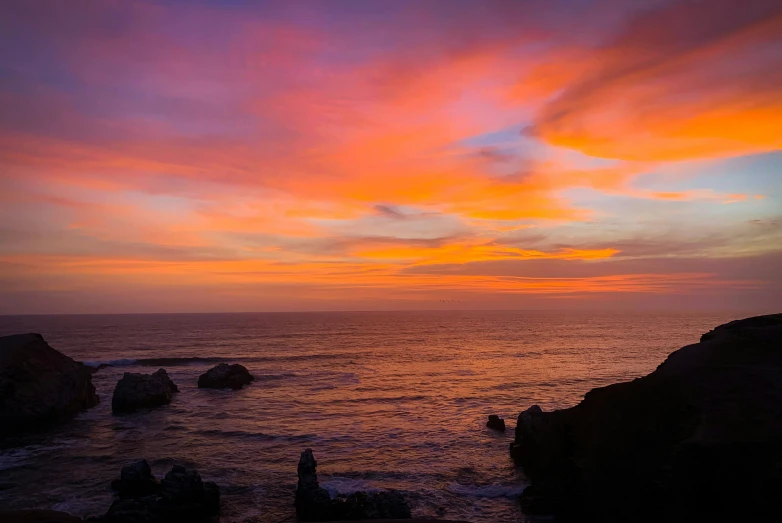 a sunset over the ocean and some rocks