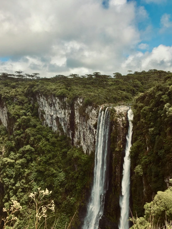 a waterfall cascading through a green jungle under a cloudy sky