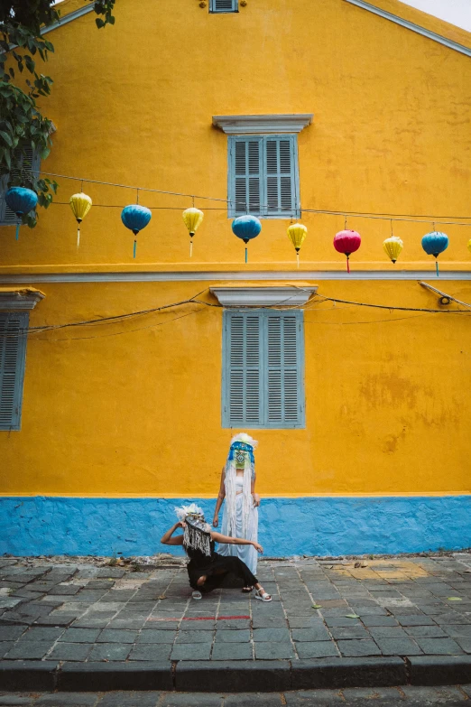 an individual sitting on the sidewalk by a yellow building