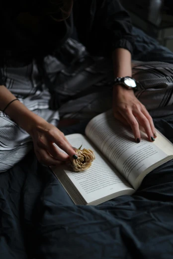 woman reading on a dark bed with the help of her hand