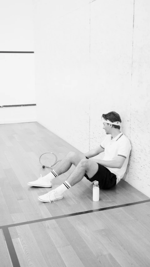 black and white pograph of young man with tennis racket sitting on the floor