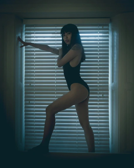the image shows a woman wearing a swimsuit leaning in front of blinds