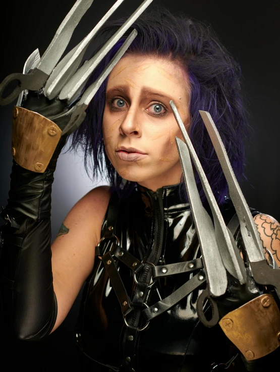 a woman in latex holds five knives in front of her head