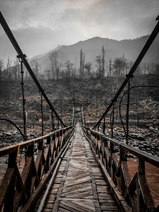 a metal bridge with a wooden footbridge on the left and a valley in the background