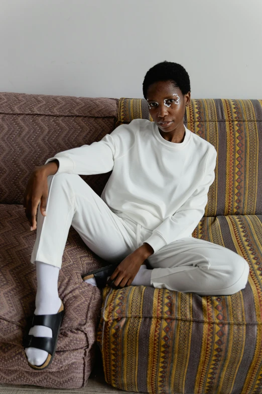 a smiling woman in white pants and sweater sitting on the couch