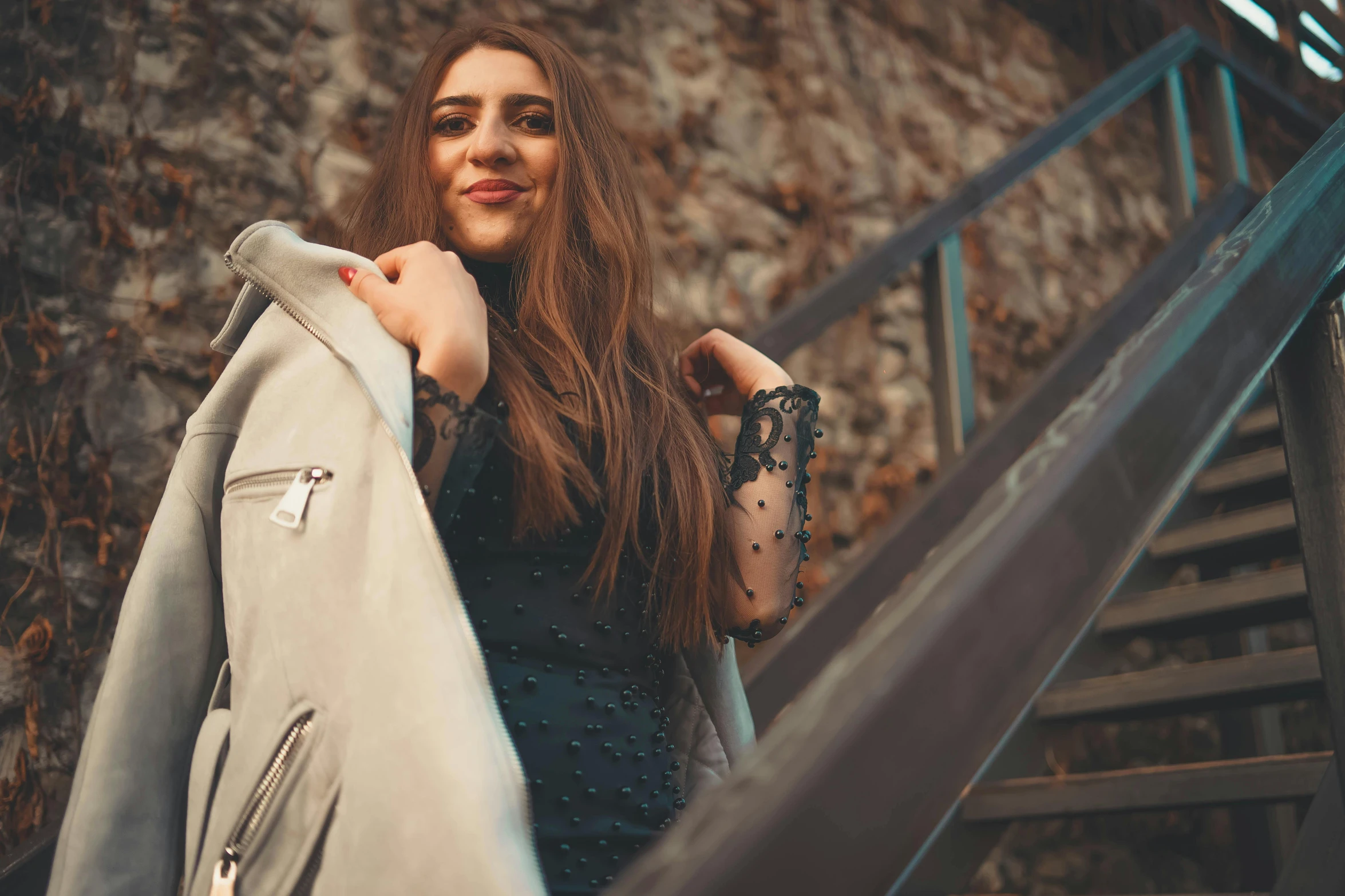 a woman in black top holding her jacket up next to some stairs