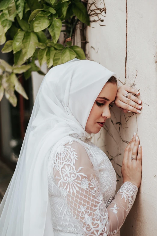 a woman in a veil and bridal veil standing against a wall
