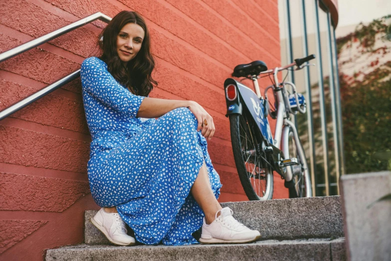 a woman sitting on stairs next to a bicycle leaning against a red wall