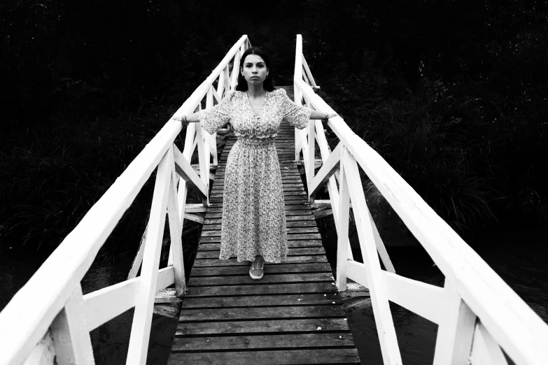 a woman in a dress stands on a bridge