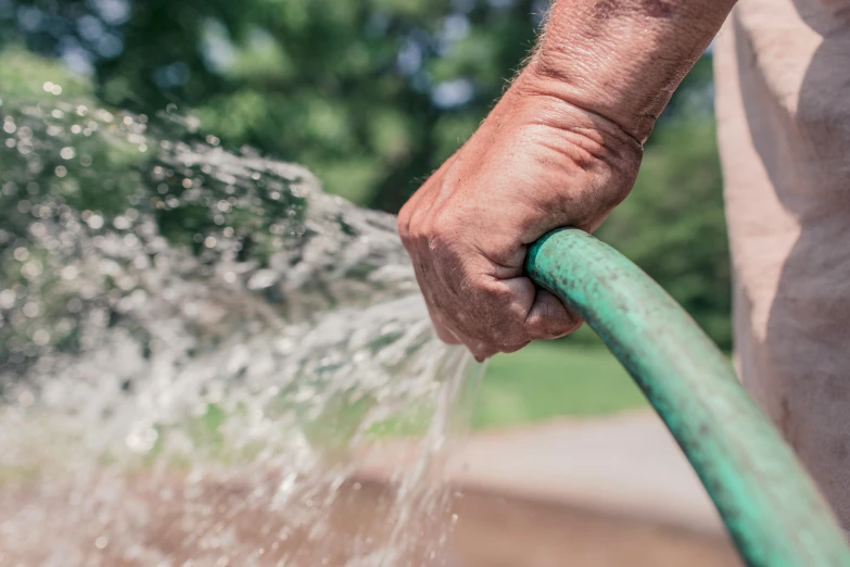 a person is holding an open hose, spraying water into the street