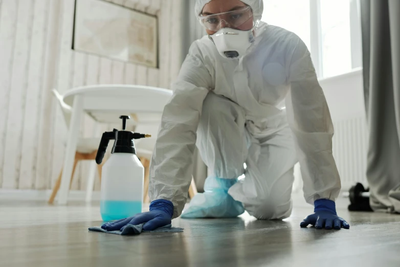 a man in white jumpsuit on floor next to a cleaner spray and gloves