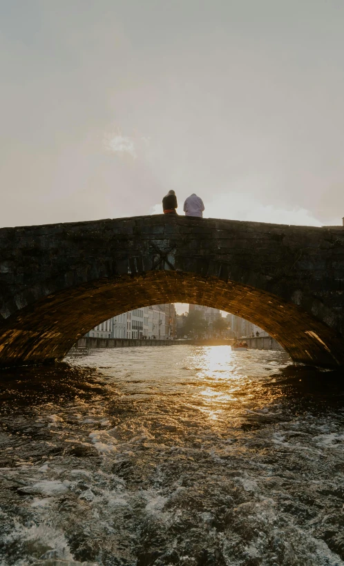 two people are sitting on the bridge over the water