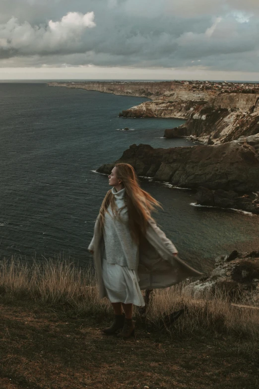 a girl dressed in white standing on a cliff