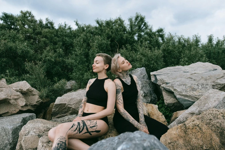 two women with tattoos sitting on rocks