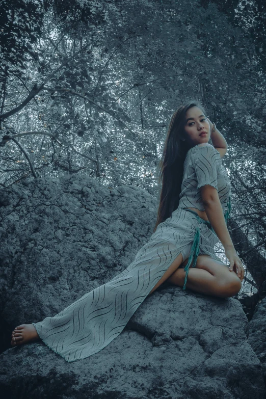 a woman in a long dress sits on a rock