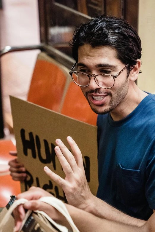 the man in glasses is talking to someone while holding a brown book