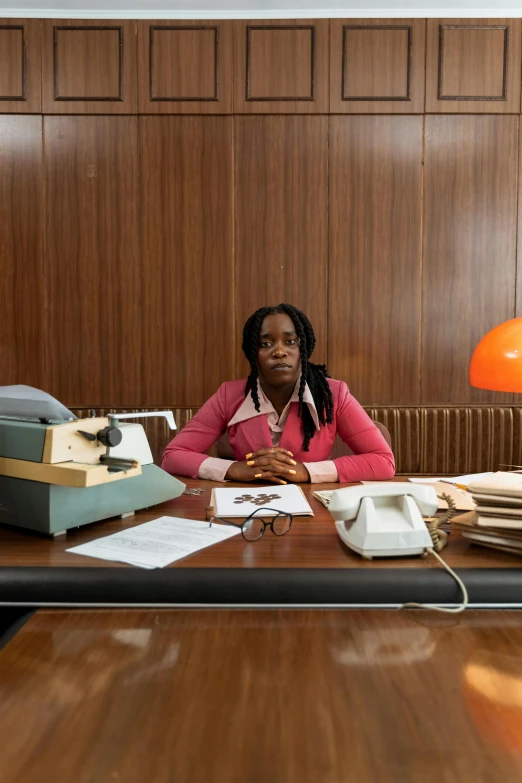 woman seated at a desk with many papers and phones