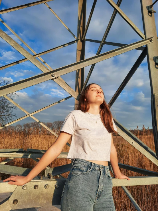 a woman standing against the metal structure looking up at a sky