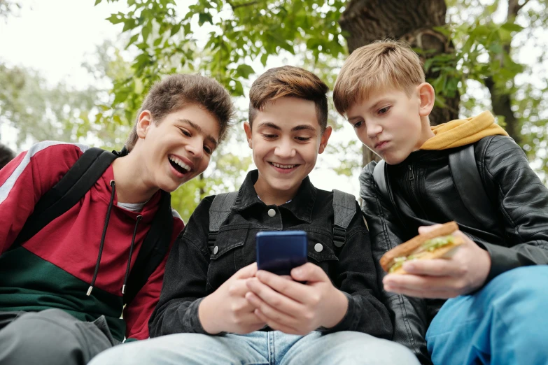 three boys standing beside each other and looking at a phone