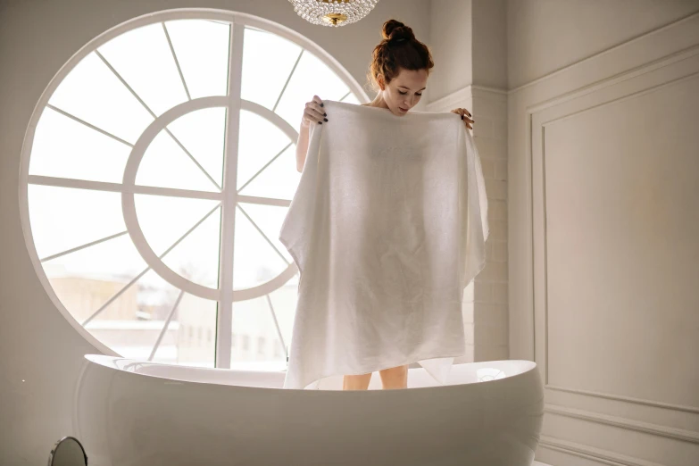 a woman is standing in a bathtub holding a towel over her head