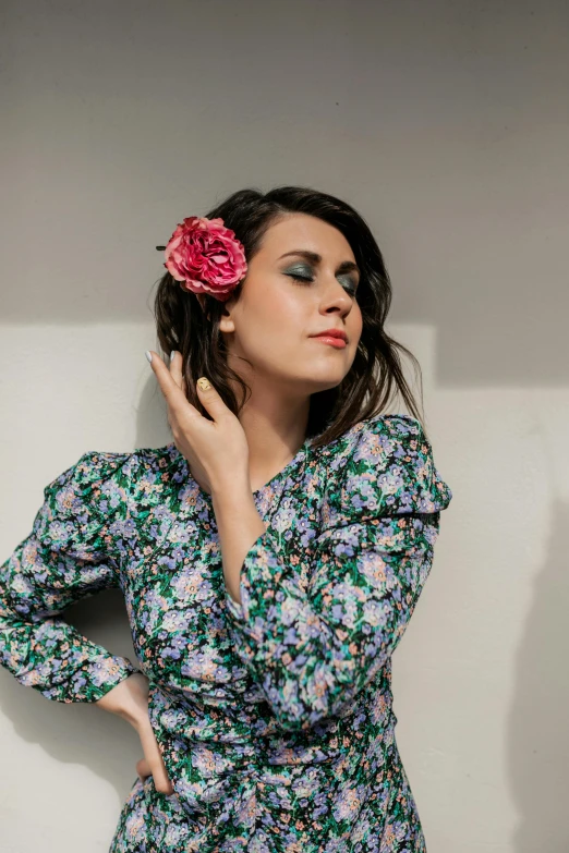 a women who is leaning against a wall with her hand on her chin and a flower in her hair