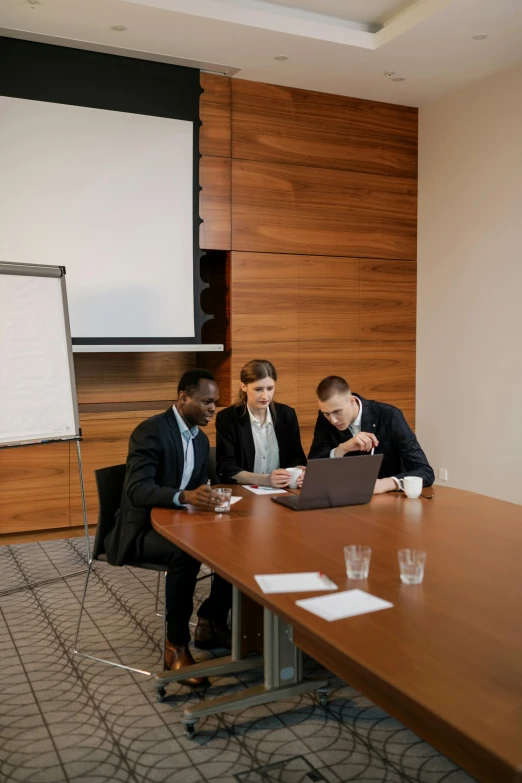 three men sitting at a table looking at a laptop