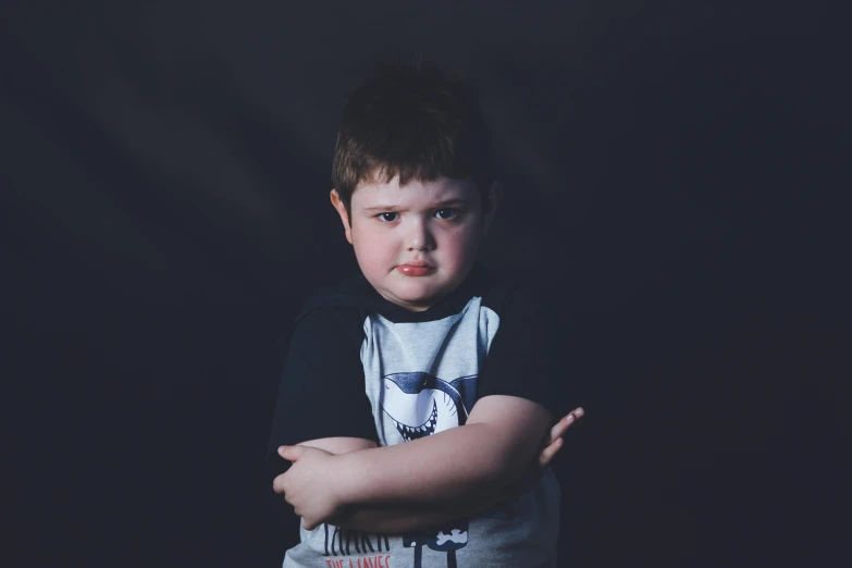 a small child with his arms crossed in a black background