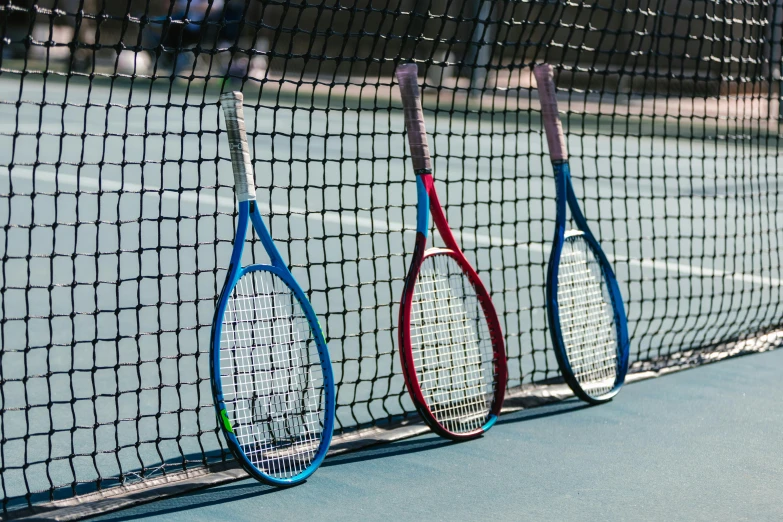 four tennis racquets leaning on the fence of a tennis court