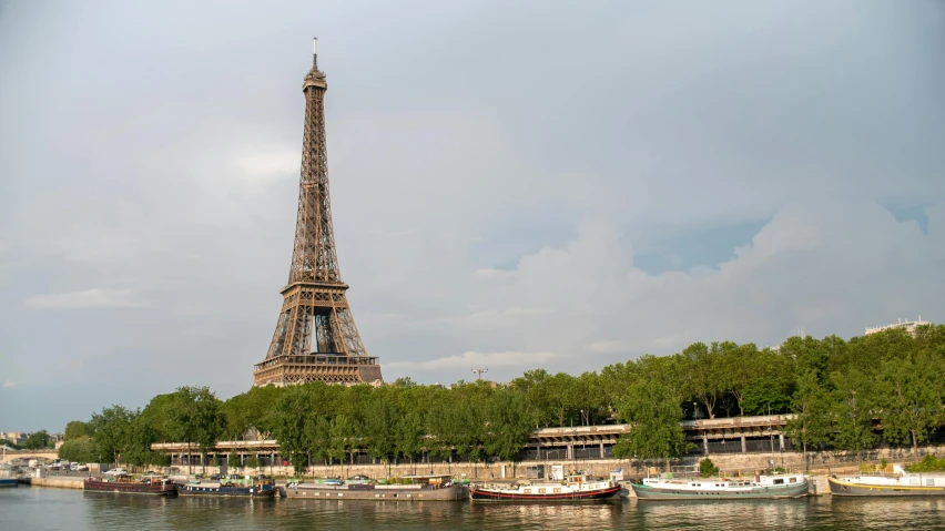 a tower with a spire in the background of some boats and trees