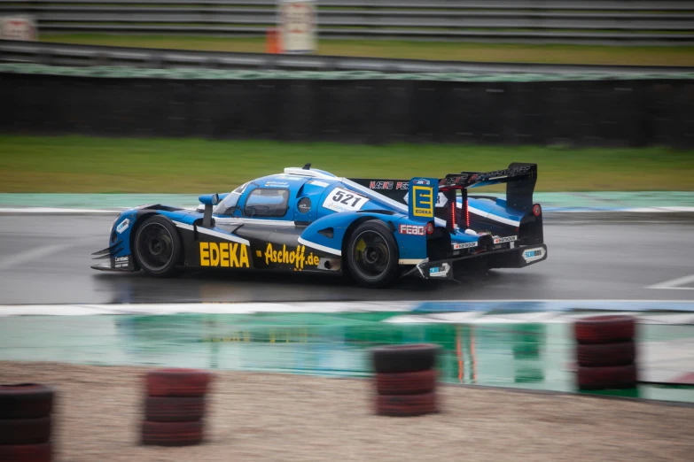 blue race car drives down the track in rain