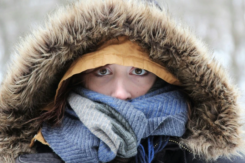 a person in a coat is covering their face with a scarf and a scarf around their neck