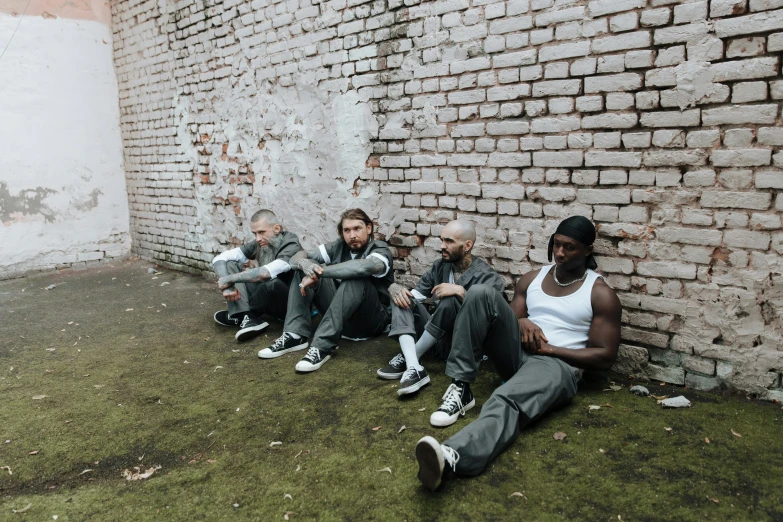 group of four people sitting on the grass by a brick wall