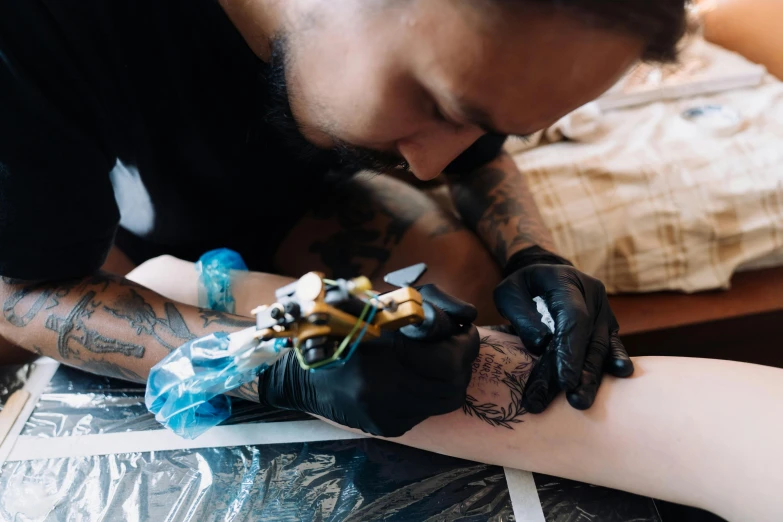 a man is getting his arm tattooed while another man looks on