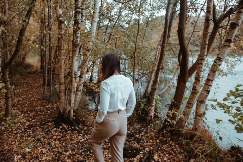 a woman standing on the edge of a river in the woods