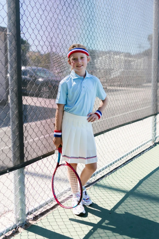 little girl in dress with tennis racket standing behind fence