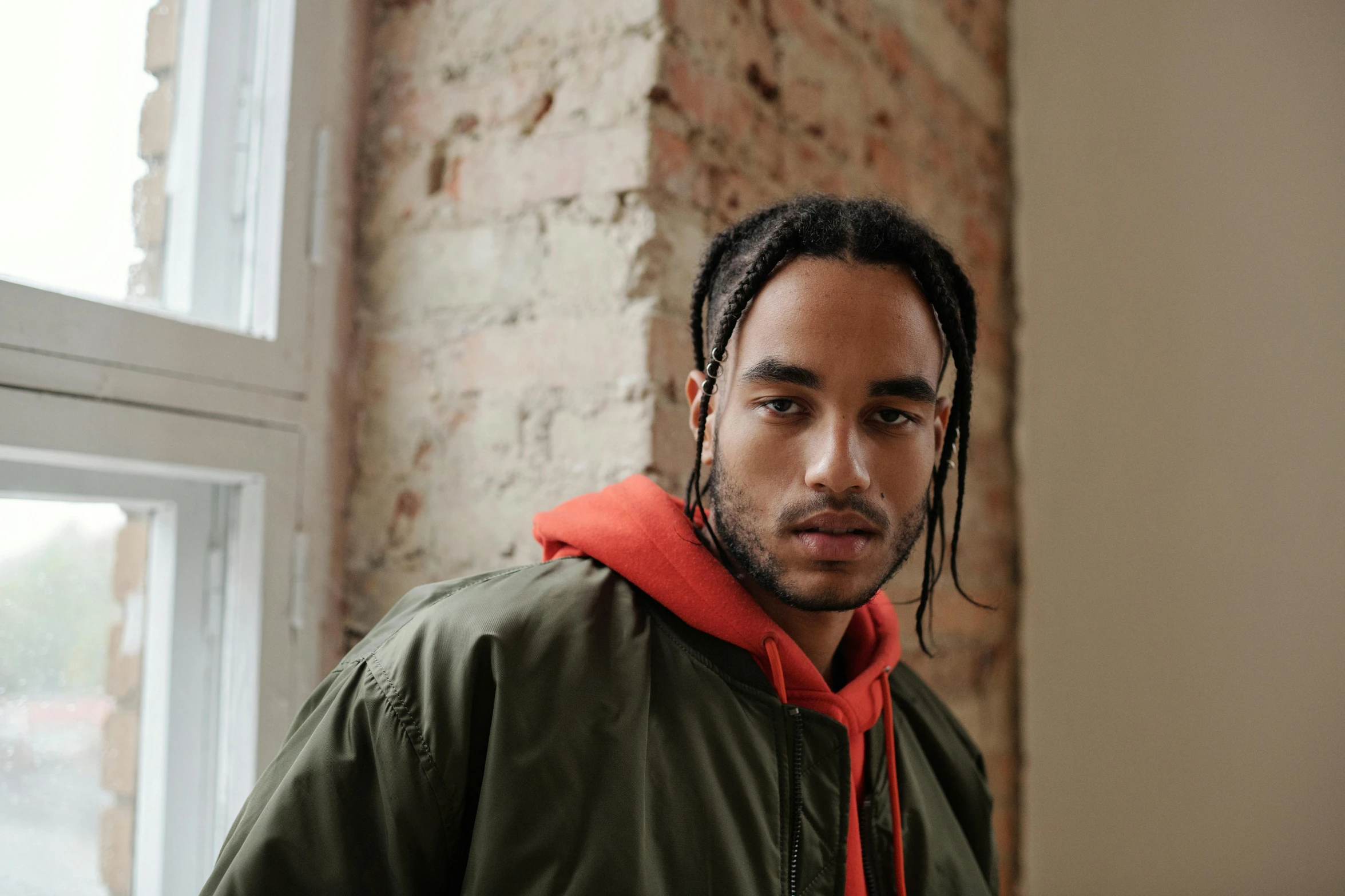 a man with dreadlocks standing in front of a brick wall