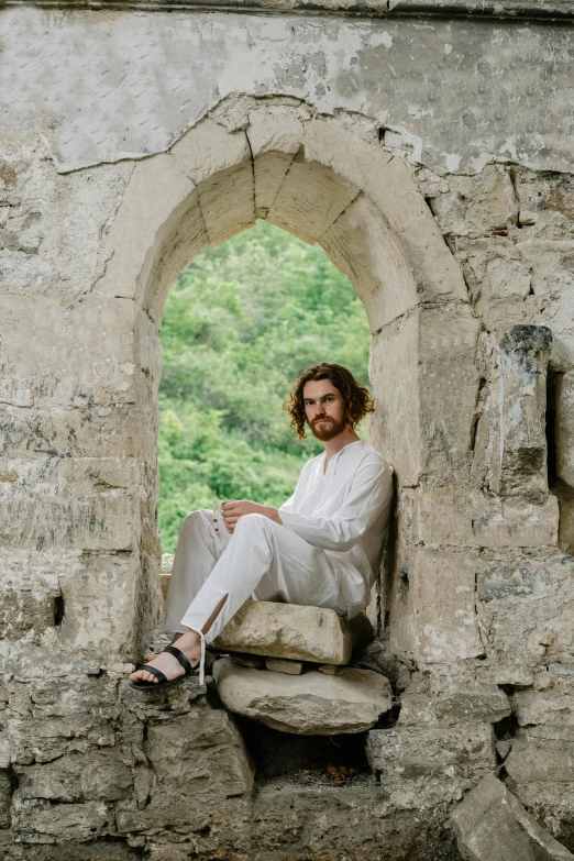 a woman sitting on top of a stone wall with her legs crossed