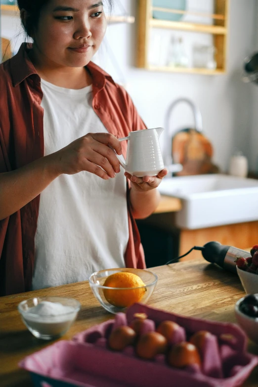 a woman pouring water into a mug next to oranges on a tray