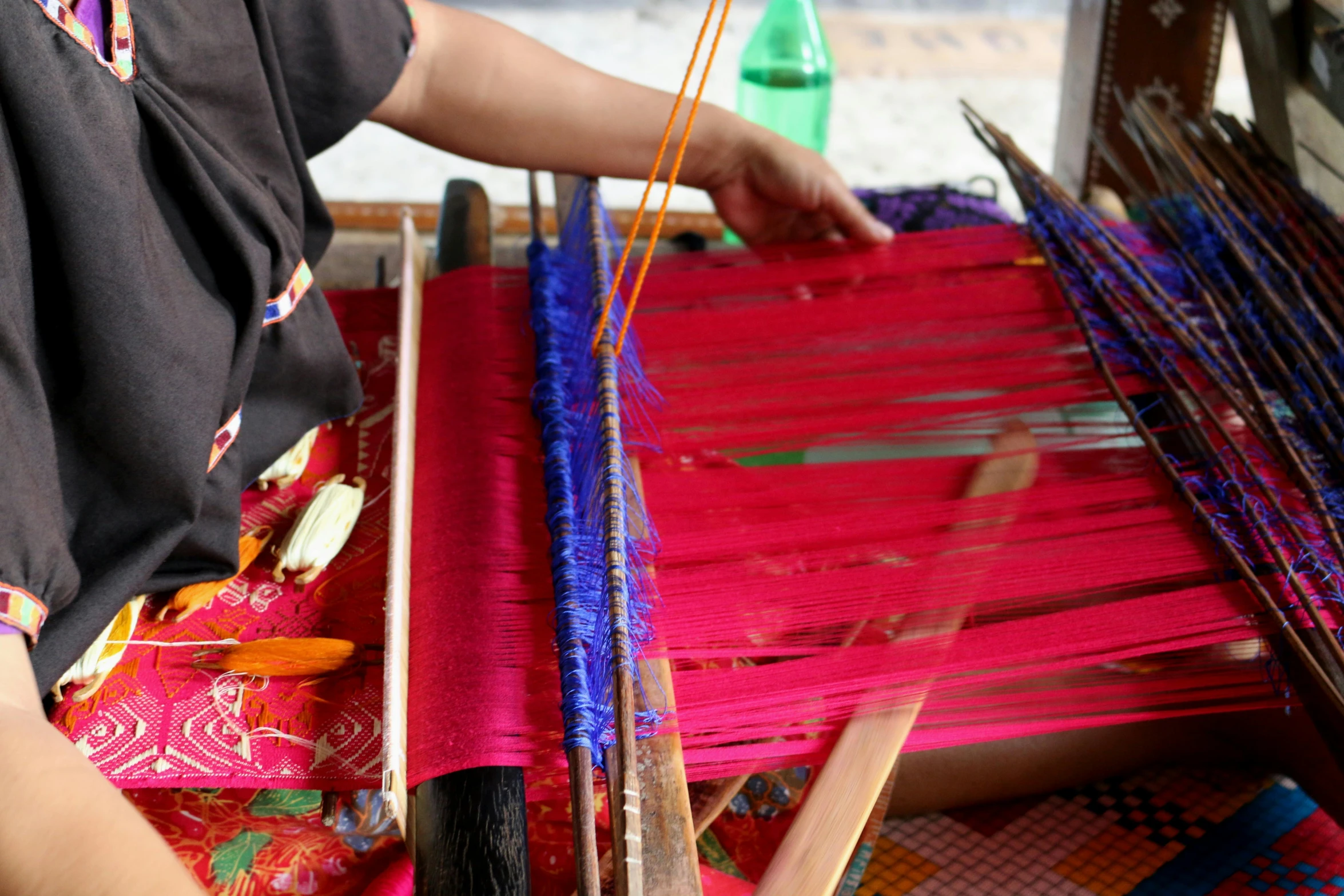 a woman is weaving a colorful blanket on an old style table