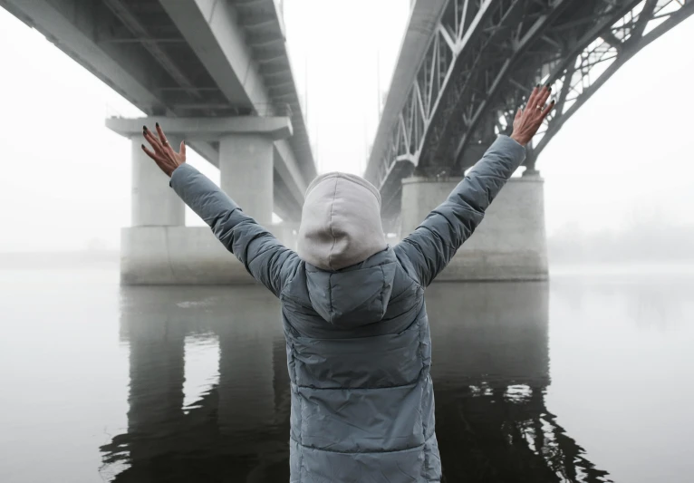 a person standing in front of a river under a bridge