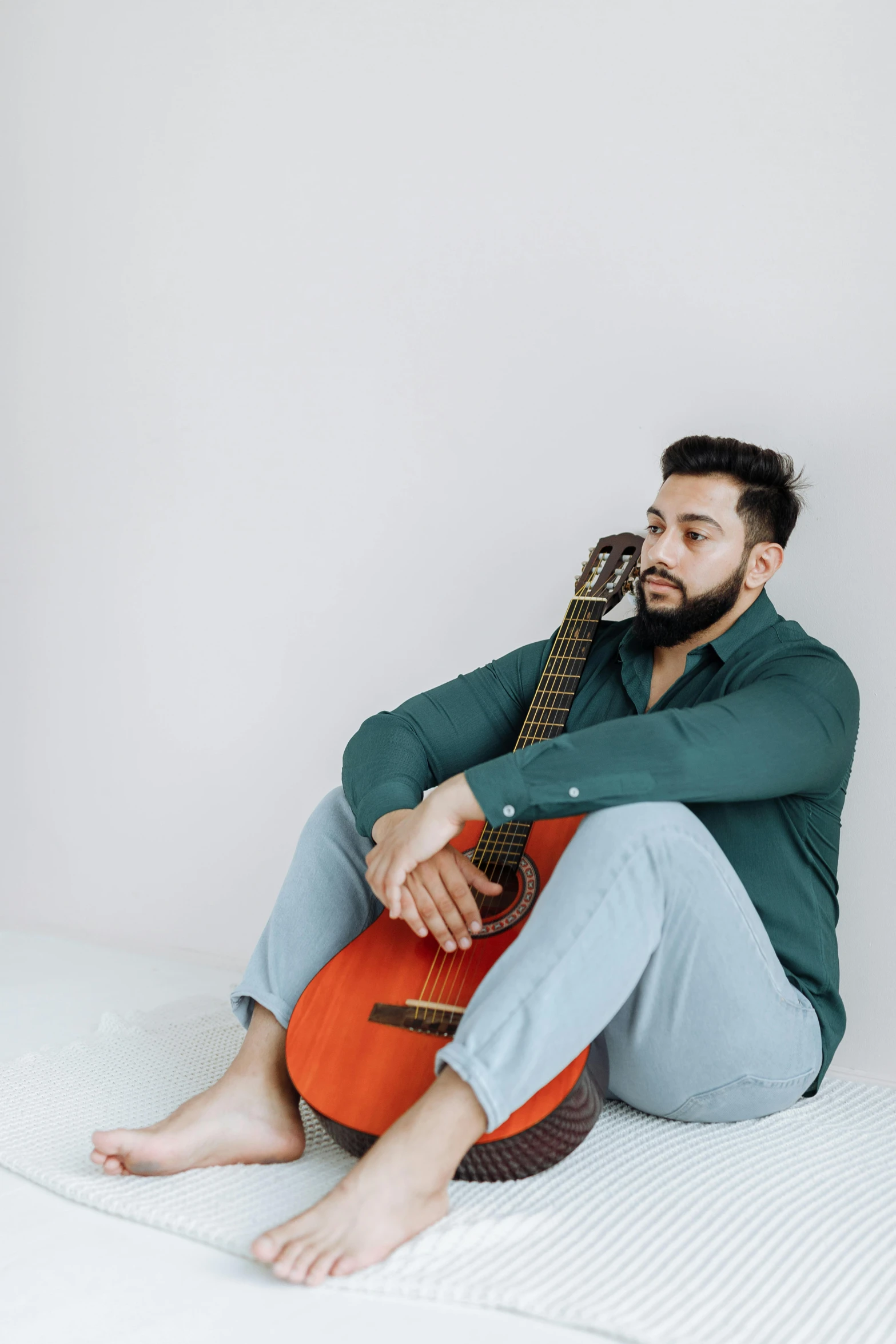 the man is sitting on his bed playing an acoustic guitar