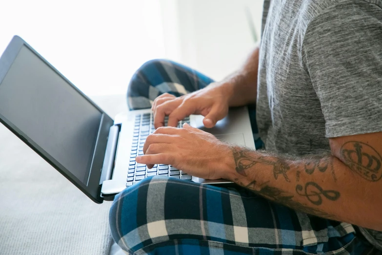 man with tattoo using his laptop computer sitting on the bed