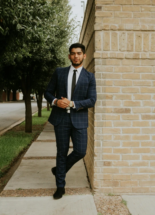 man in suit and tie leaning up against a wall on concrete sidewalk