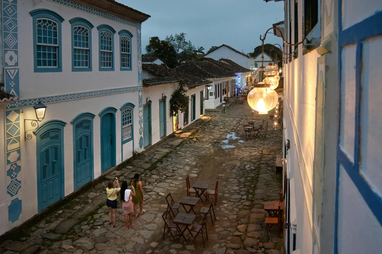 people walk down a cobblestone street with white buildings in the background